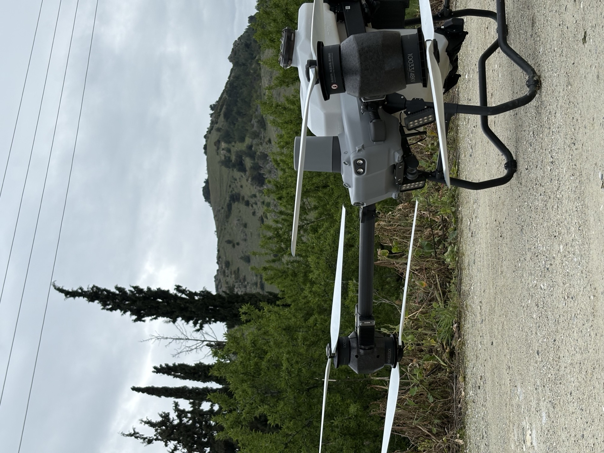 Το DJI Agras T50 φορτωμένο στο τρέιλερ, με κυπαρίσσια και λόφο στο βάθος